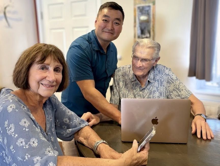 John Wang giving patient, in-person tech support to senior clients on their laptop